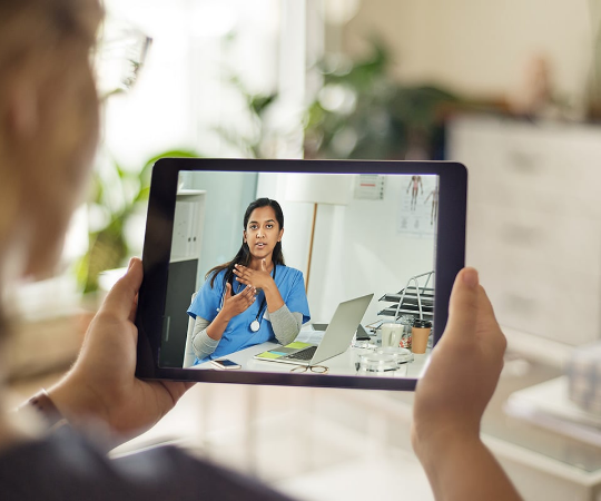 Picture: Woman with glasses holding tablet while on video call with doctor