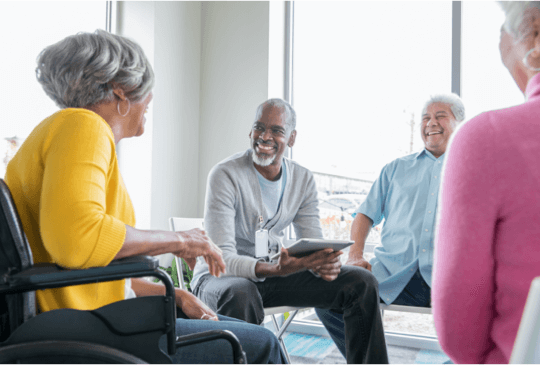 group of men and women sitting in circle of chairs smiling and talking
