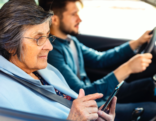 Picture: Woman with glasses in passenger seat of car looking at her phone while her son drives