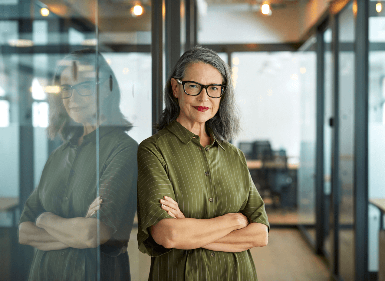 Woman wearing glasses standing in office with arms crossed and smiling