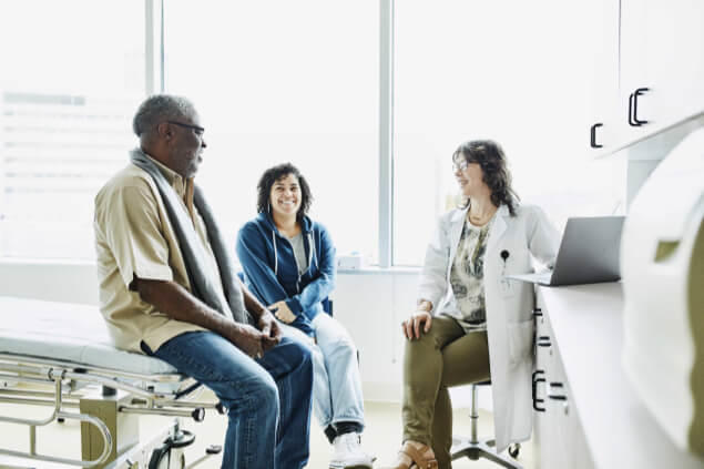 Female doctor, male patient and female caregiver speaking in examination room