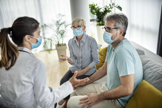 Female nurse speaking with patient and caregiver, all wearing face masks