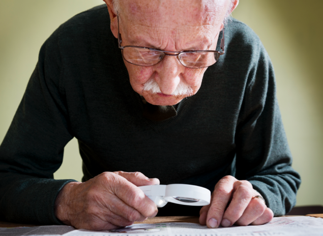 Older man with glasses using magnifying glass to read on desk