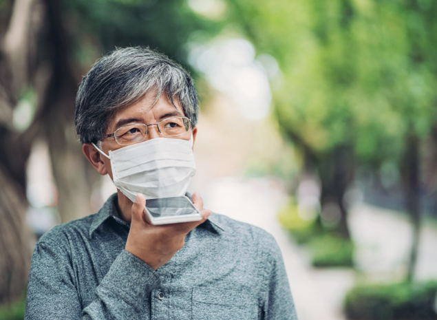 Man with glasses and mask on speaking into smartphone outside